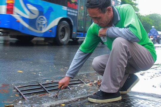 Ảnh: Tài xế xe ôm khơi thông cống thoát nước sau trận mưa lớn ở Hà Nội